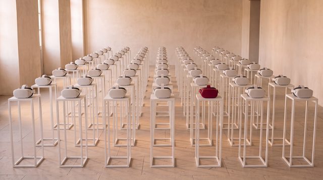 Rows of white VR headsets on white plinths, one red