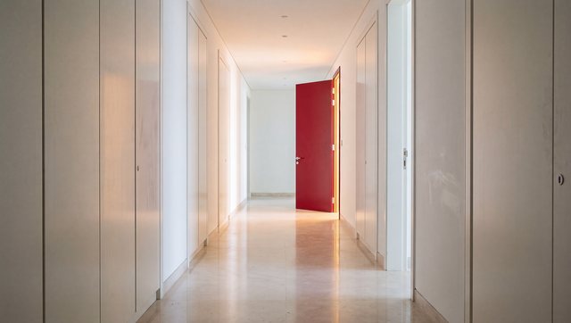 A white corridor of closed doors, one red door standing open
