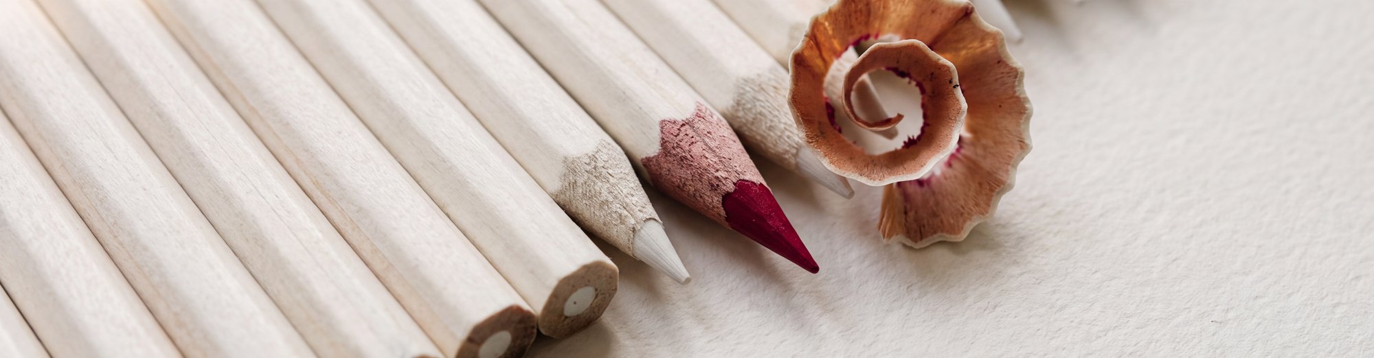 A row of white pencils, one sharpened to a red point